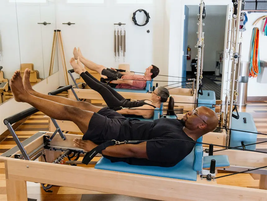 pilates-classes-huntsville A group of men and women foing the Hundred exercise on the Reformer during a Reformer Pilates class in Huntsville AL